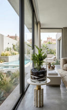 Charger l'image dans la galerie, Terrarium cylindre XL avec strates de sable et galets posé sur une sellette en marbre dans un salon de villa moderne